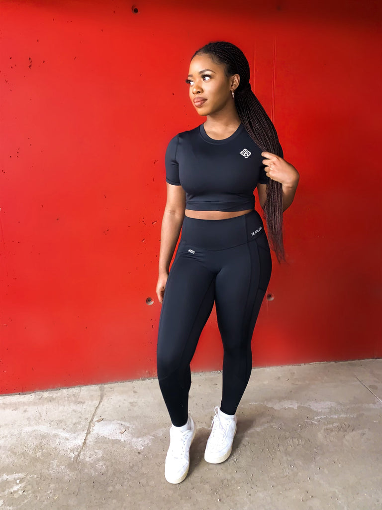 Woman wearing the Agu Crop Top and Fearless Leggings both in the colour black. The leggings are high-waisted and squat proof. Fitness. Women in fitness. Fashion