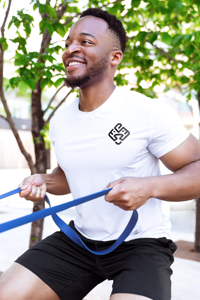 Male exercising outdoors with a resistance band. He is wearing the white premium athletic tee from Agu Athletics.