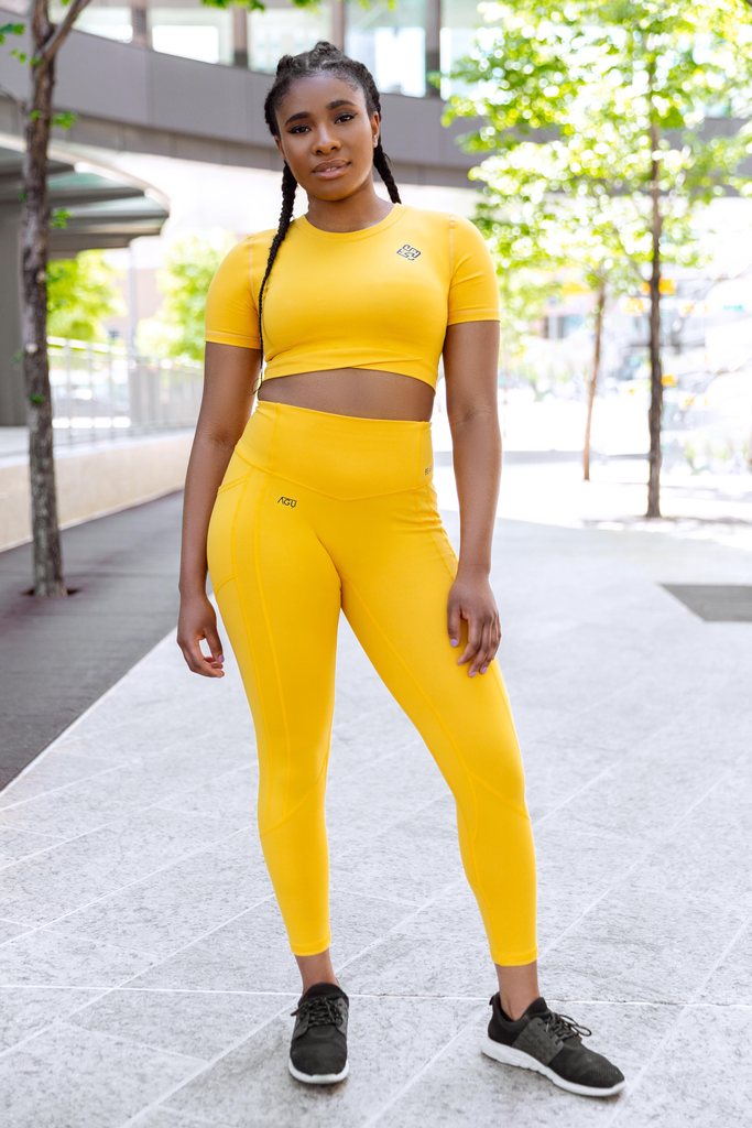 Model wearing yellow high waisted gym leggings and yellow crop top with lion logo
